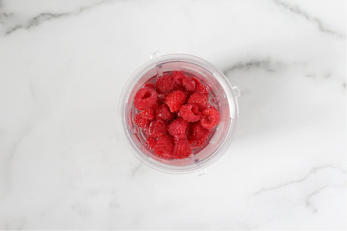Fresh raspberries in water in a blender cup.