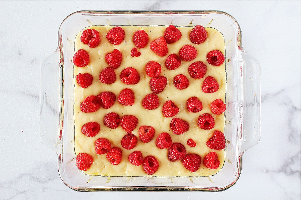 Fresh raspberries on top of cake batter in a glass pan.