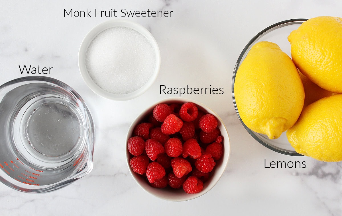 Labeled ingredients for low sugar raspberry lemonade on a white marble countertop.