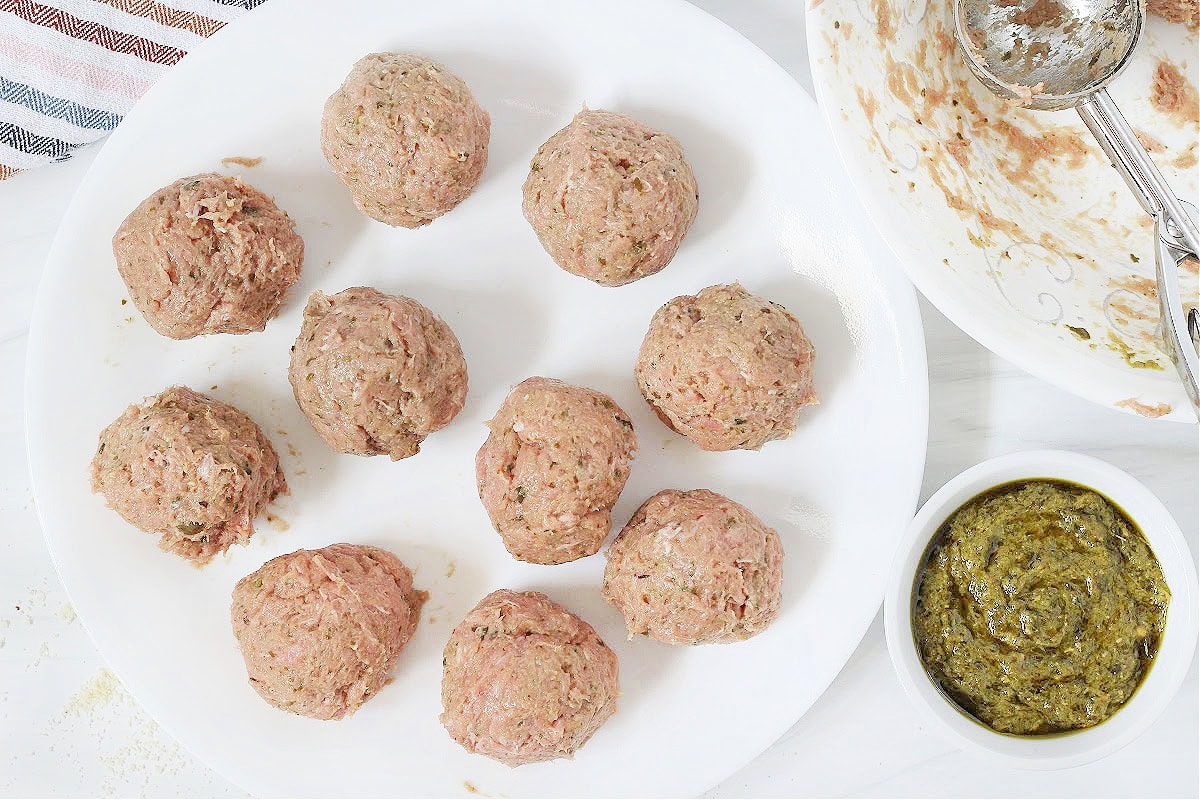 Ten unbaked turkey basil meatballs on a white plate.