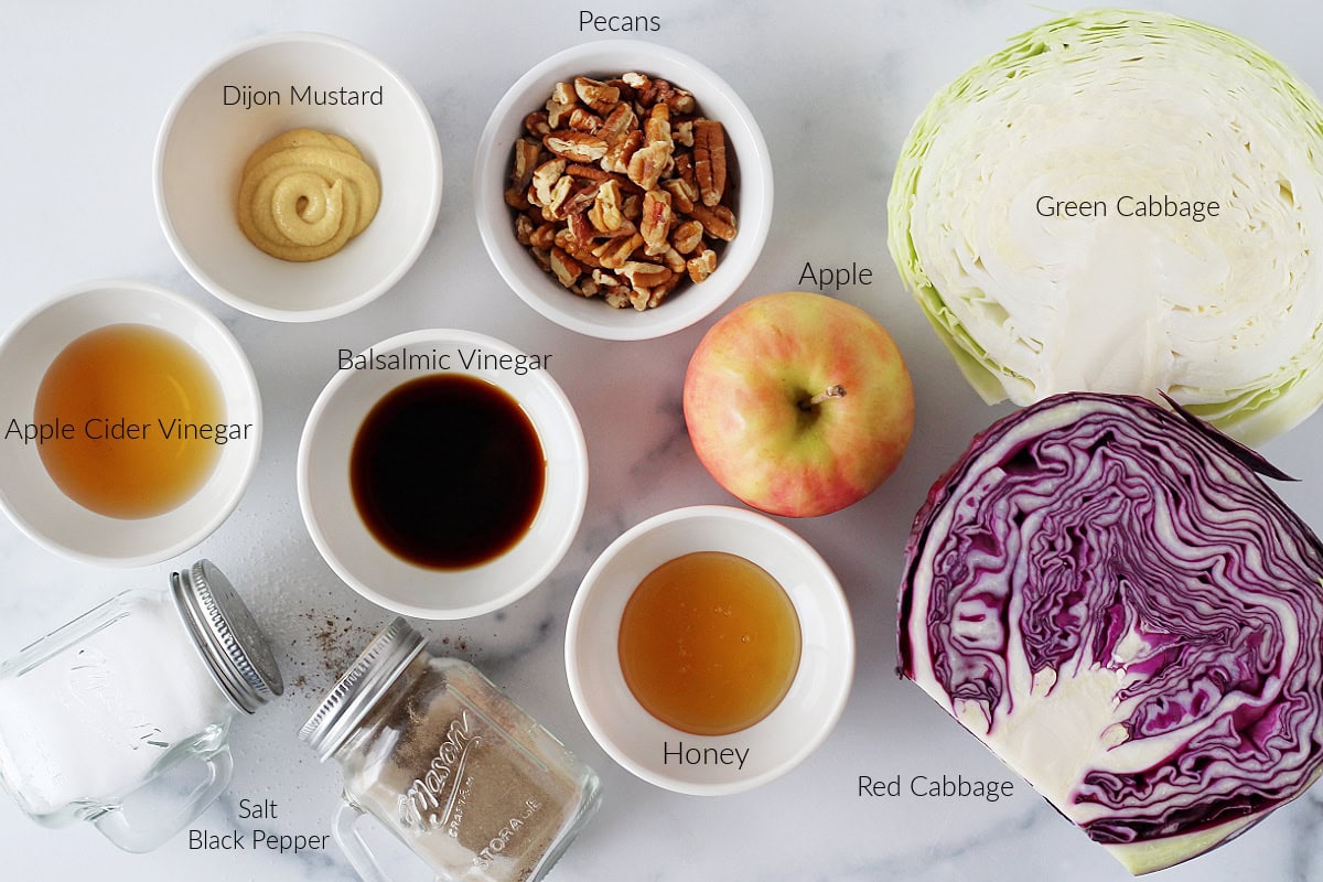 Labeled ingredients for roasted cabbage and apple salad on a white marble countertop.