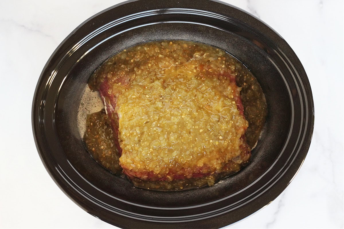 Salsa verde covering a roast in a crock pot.