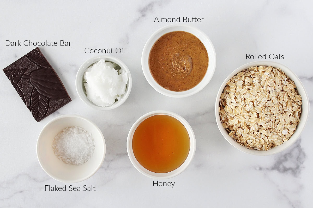 Labeled ingredients for salted dark chocolate granola on a white marble countertop.
