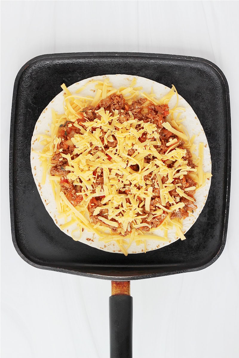 An open faced sloppy joe quesadilla on a flat griddle pan.