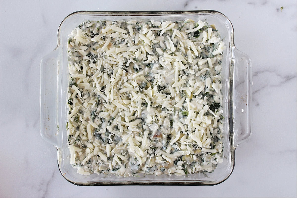 Spinach and artichoke dip in a glass pan topped with shredded mozzarella.
