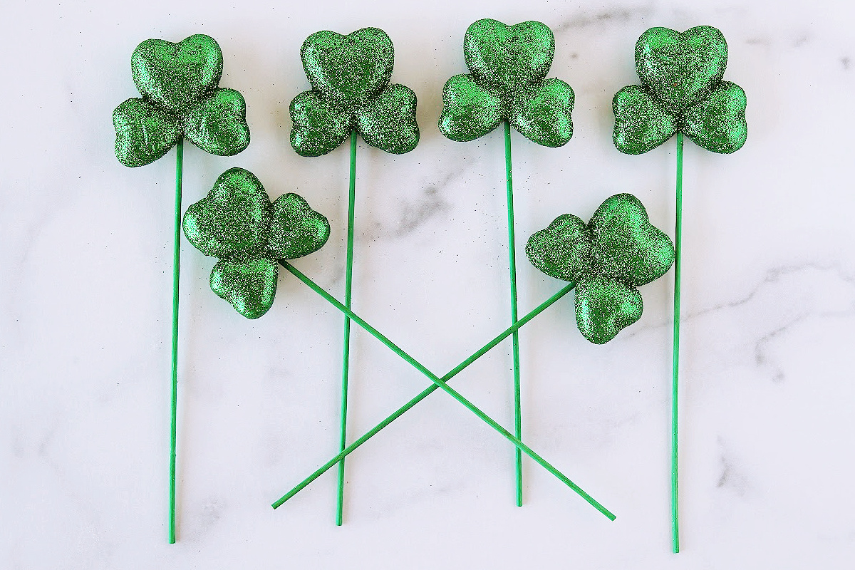 Six green sparkly kabob sticks on a white countertop.