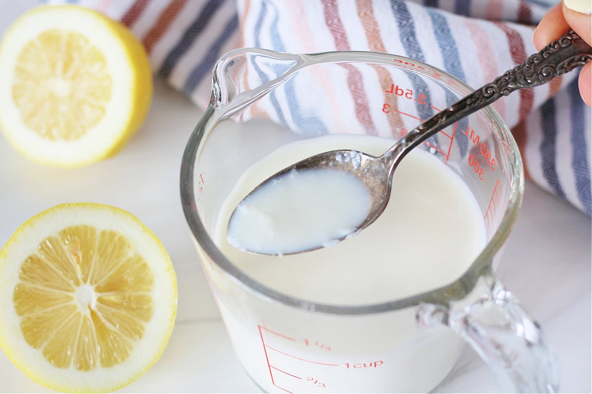 A vintage spoon with buttermilk on it over the glass measuring cup of buttermilk.