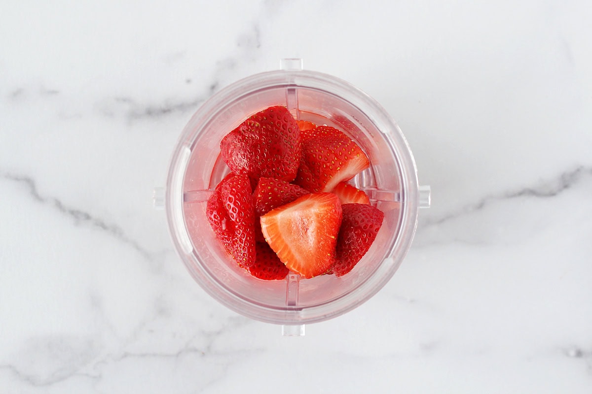 Sliced strawberries and water in a clear blender canister.