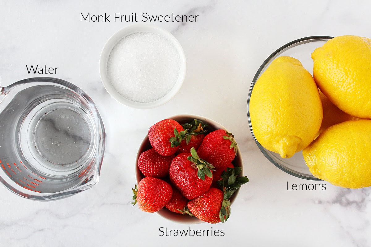 Water, monk fruit sweetener, fresh strawberries and whole lemons for a strawberry lemonade recipe.
