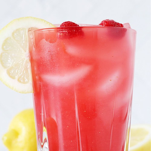 A glass of homemade raspberry lemonade with fresh raspberries and lemon slices.
