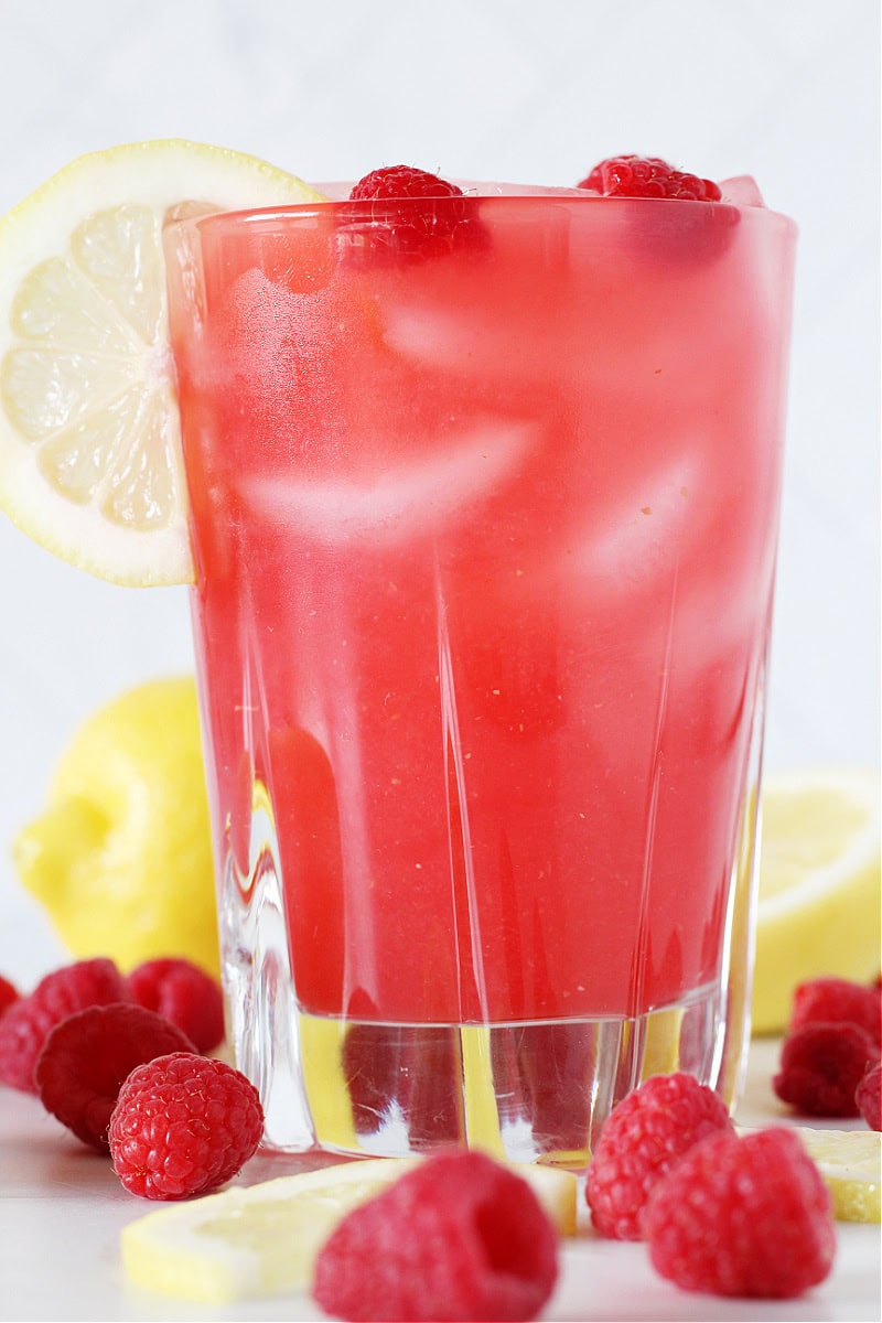A glass of homemade raspberry lemonade with fresh raspberries and lemon slices.