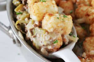Tater tots on top of a creamy ground beef mixture on a spoon.