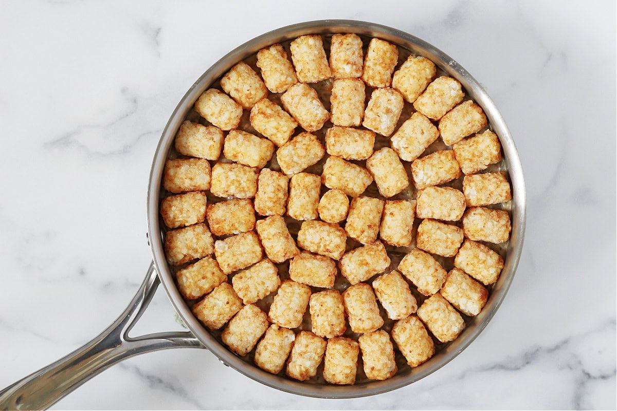Tater tots on top of a meat green bean mixture.