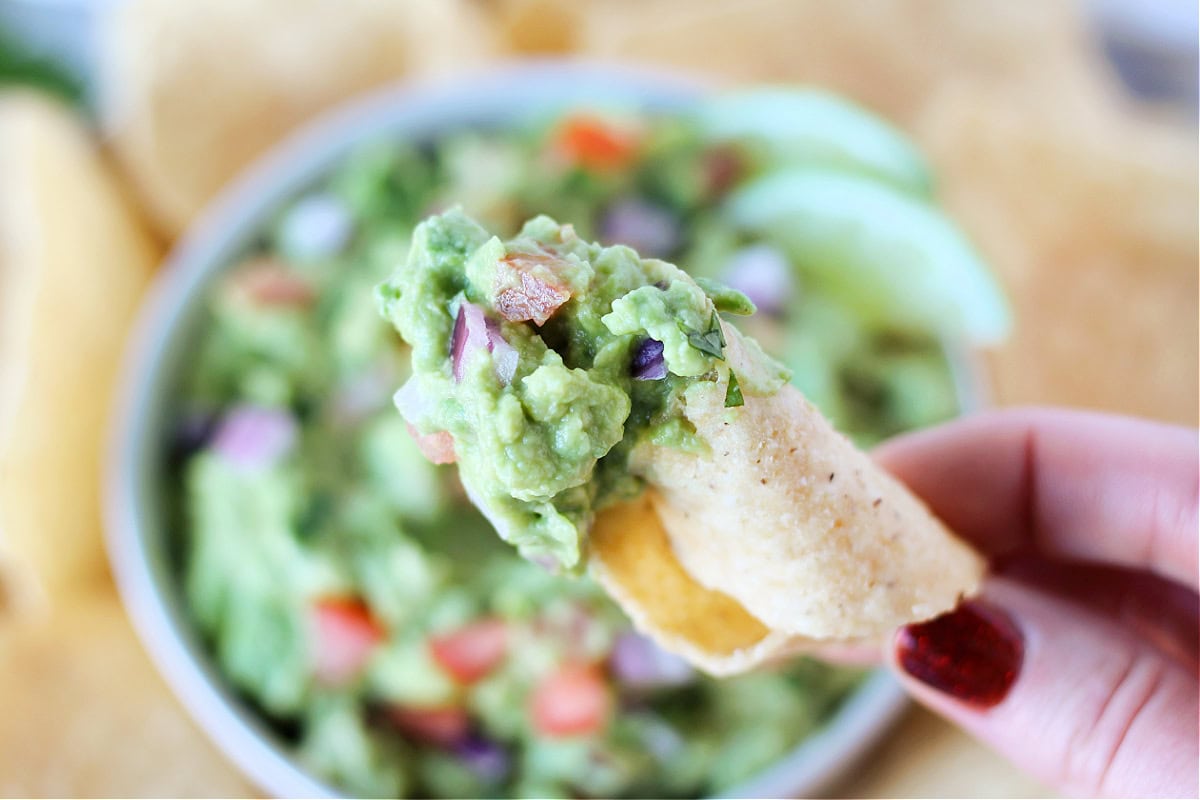 A woman's fingers holding a tortilla chip with homemade guacamole on it.