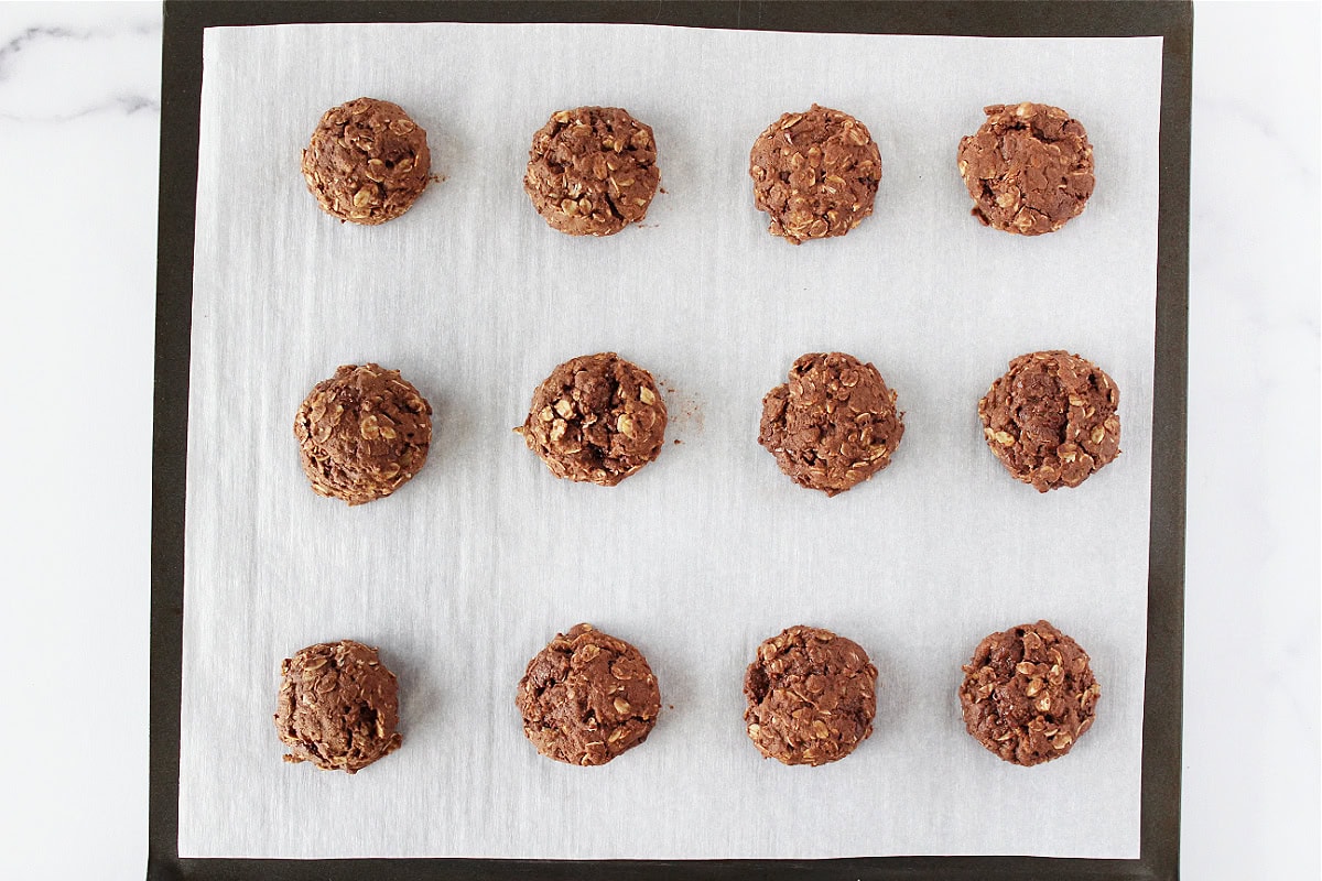 Twelve baked chocolate oatmeal cookies on parchment paper on a baking sheet.