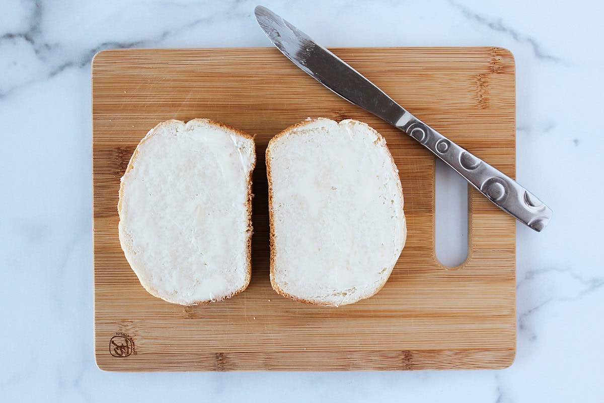 Two slices of bread with butter spread on top on a wooden cutting board.