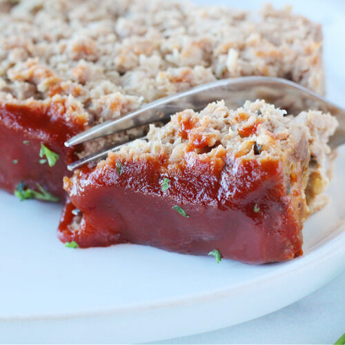A fork slicing into a piece of meatloaf topped with a ketchup sauce.