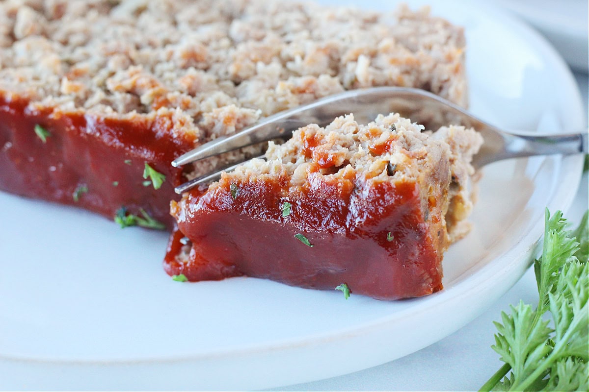 A fork slicing into a piece of meatloaf topped with a ketchup sauce.