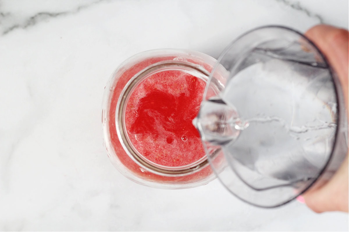 Pouring water into a glass mason jar with raspberry lemonade concentrate.