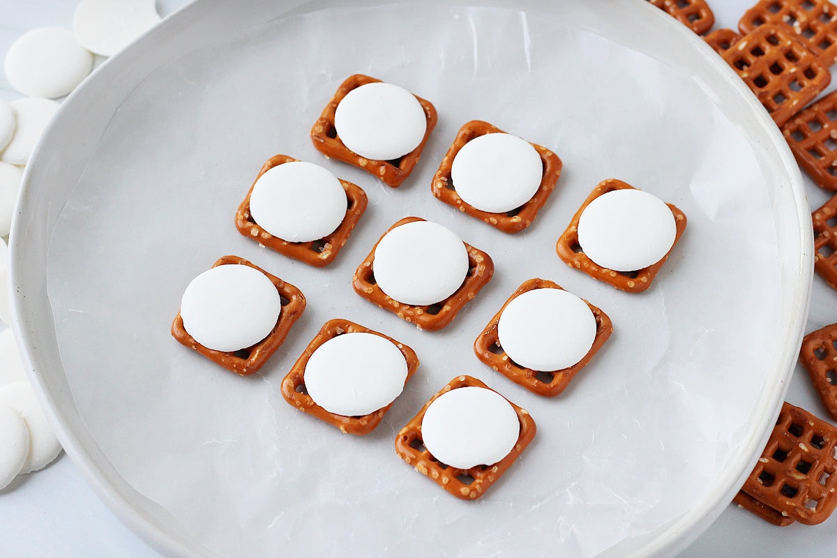 Nine square pretzels with white candy wafers on top on a plate.