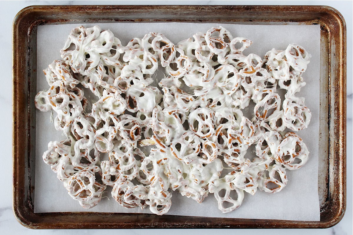 Pretzels coated in melted white chocolate on a parchment lined baking sheet.