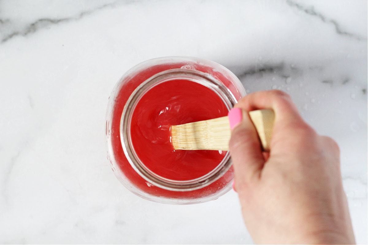 A woman's hand using a wooden spoon to stir raspberry lemonade in a glass jar.