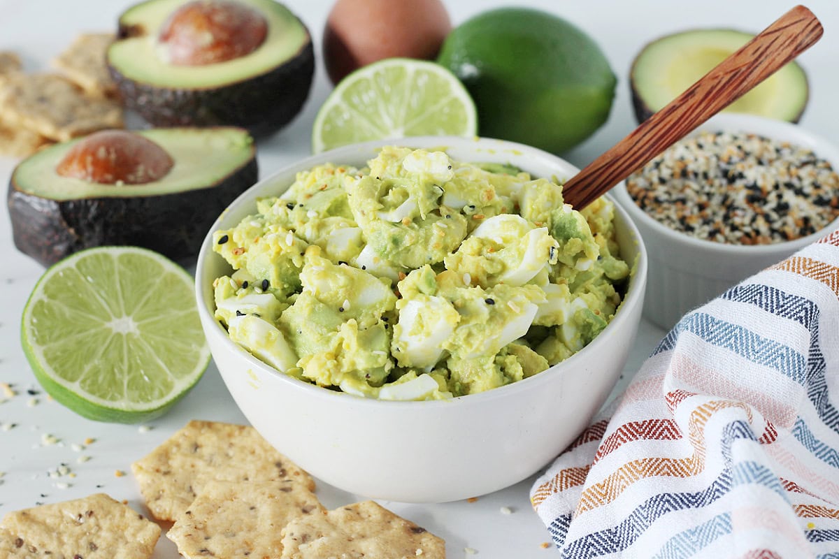A bowl of avocado egg salad with a wooden spoon sticking out.