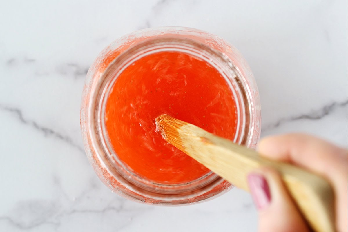A wooden spoon stirring a strawberry lemonade recipe in a large glass mason jar.