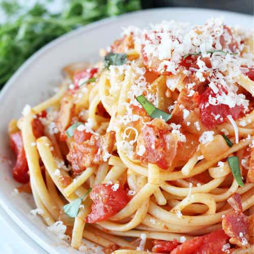 Homemade Pasta All’Amatriciana on a white plate topped with cheese.