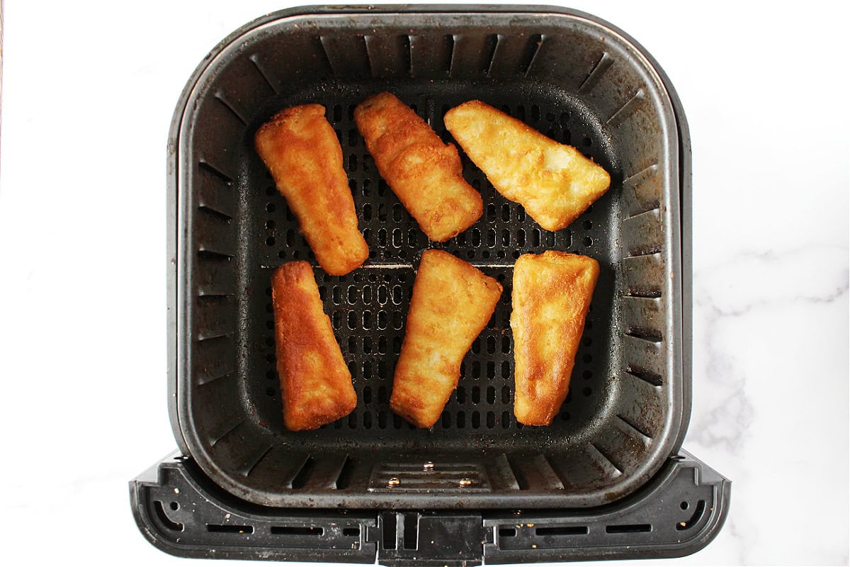 Six golden brown beer battered fish filets in an air fryer basket.