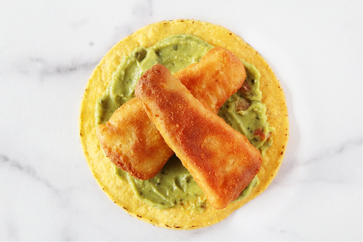 Two golden brown battered fish filets on top of guacamole and a tostada shell.
