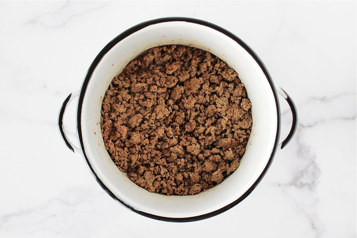 Browned ground beef in a white soup pot.