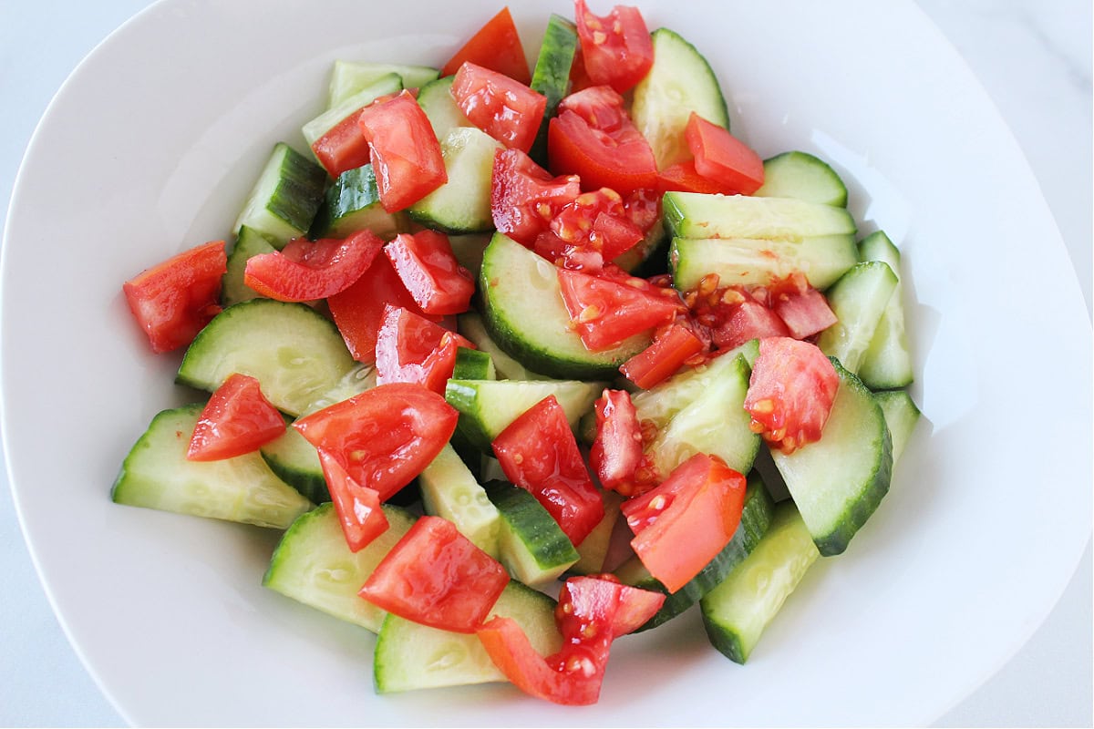 Diced cucumbers and tomatoes in a white bowl.