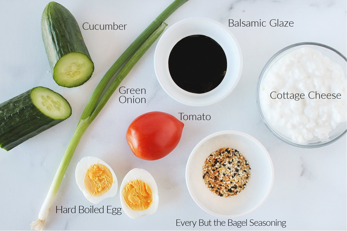 Labeled ingredients for cottage cheese cucumber salad with hard boiled eggs and veggies.