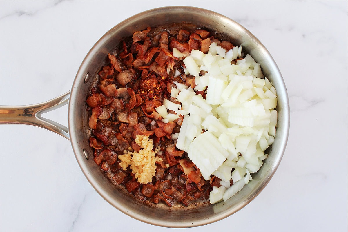 Chopped onion and minced garlic on top of cooked bacon pieces.
