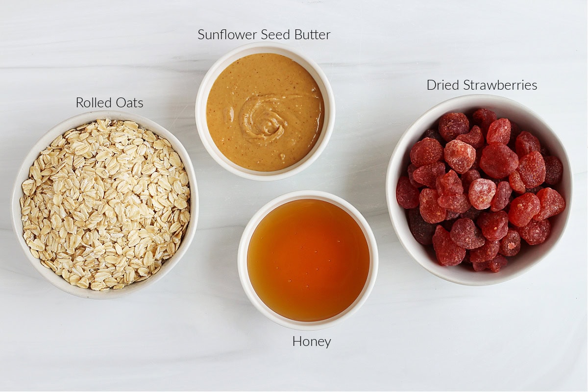 Labeled ingredients for peanut butter and jelly energy bites on a white marble countertop.