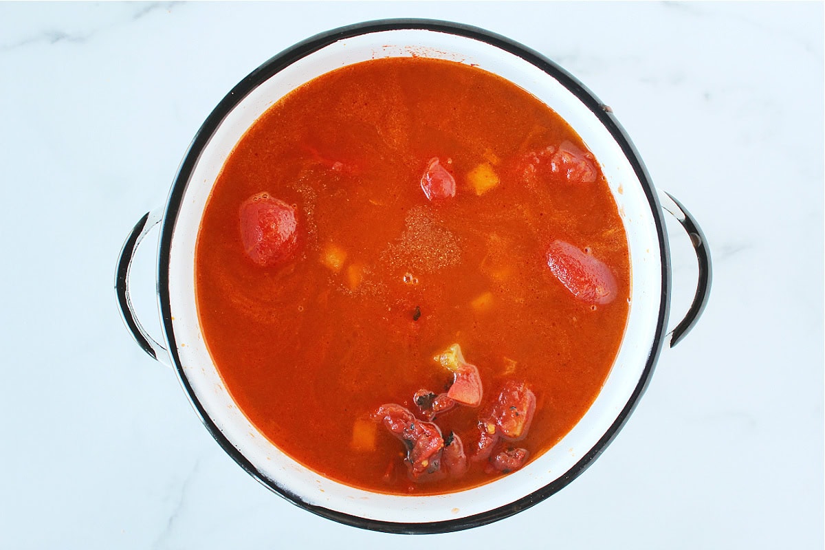 Fire roasted tomatoes and canned whole tomatoes in a white soup pot.