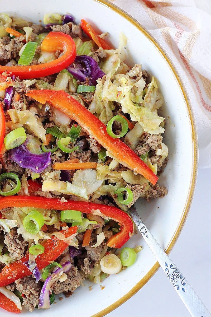 A fork in a white bowl filled with egg roll in a bowl.