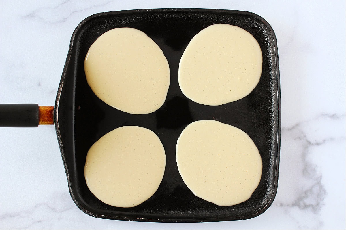 Batter poured into four pancake shapes on a black stovetop skillet.