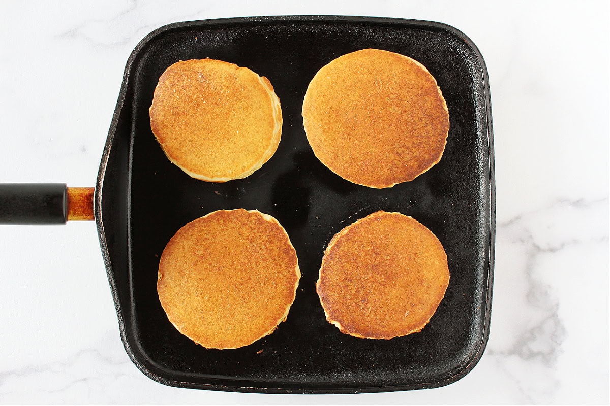 Four golden pancakes cooked on a black stovetop pan.