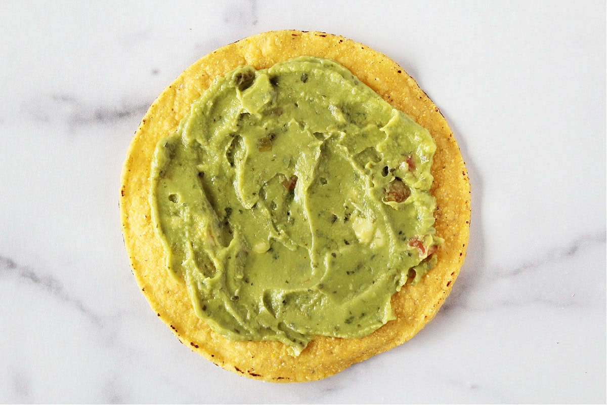 A tostada shell with guacamole spread in a thin layer on top.