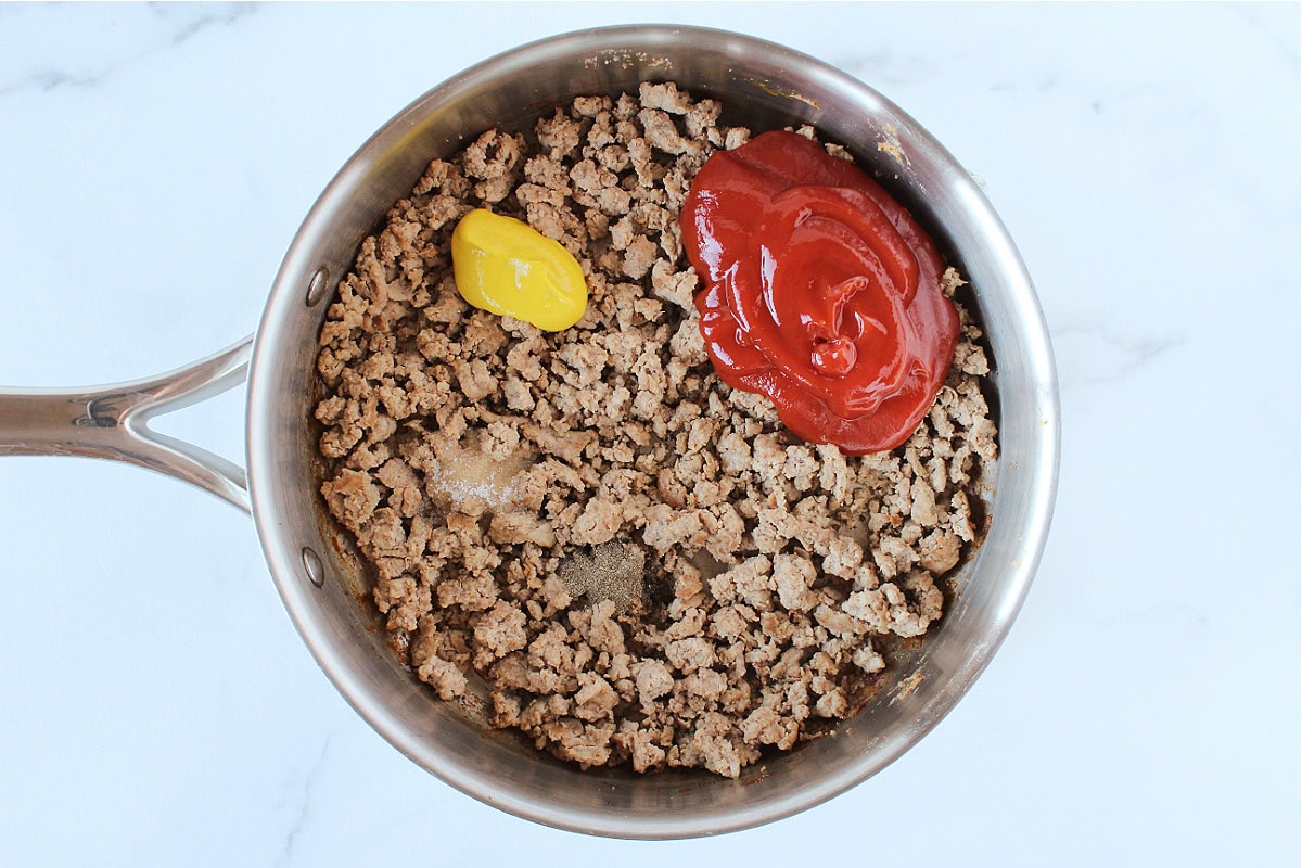 Browned ground meat with ketchup, mustard, salt and black pepper on top.