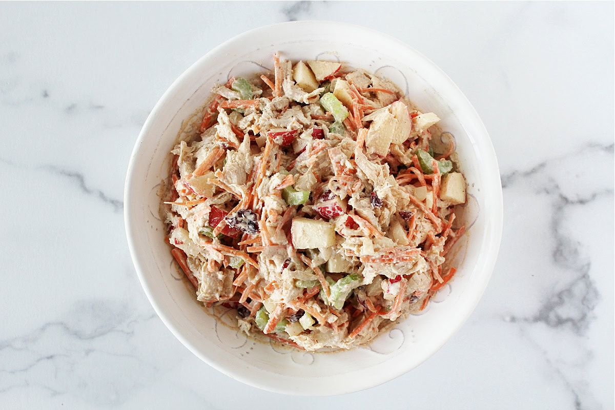 Shredded carrots, apples, celery and turkey mixed with a yogurt dressing in a bowl.
