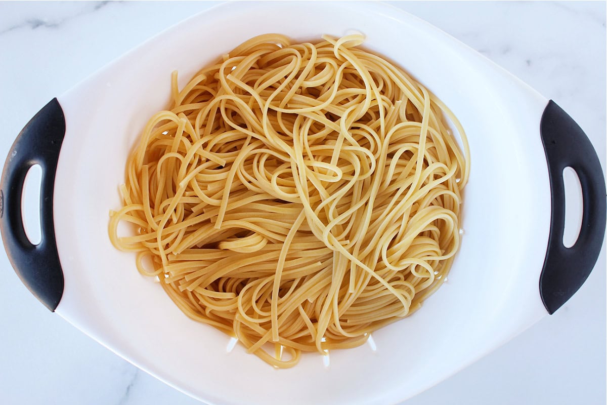 Cooked linguine pasta in a white pasta strainer.
