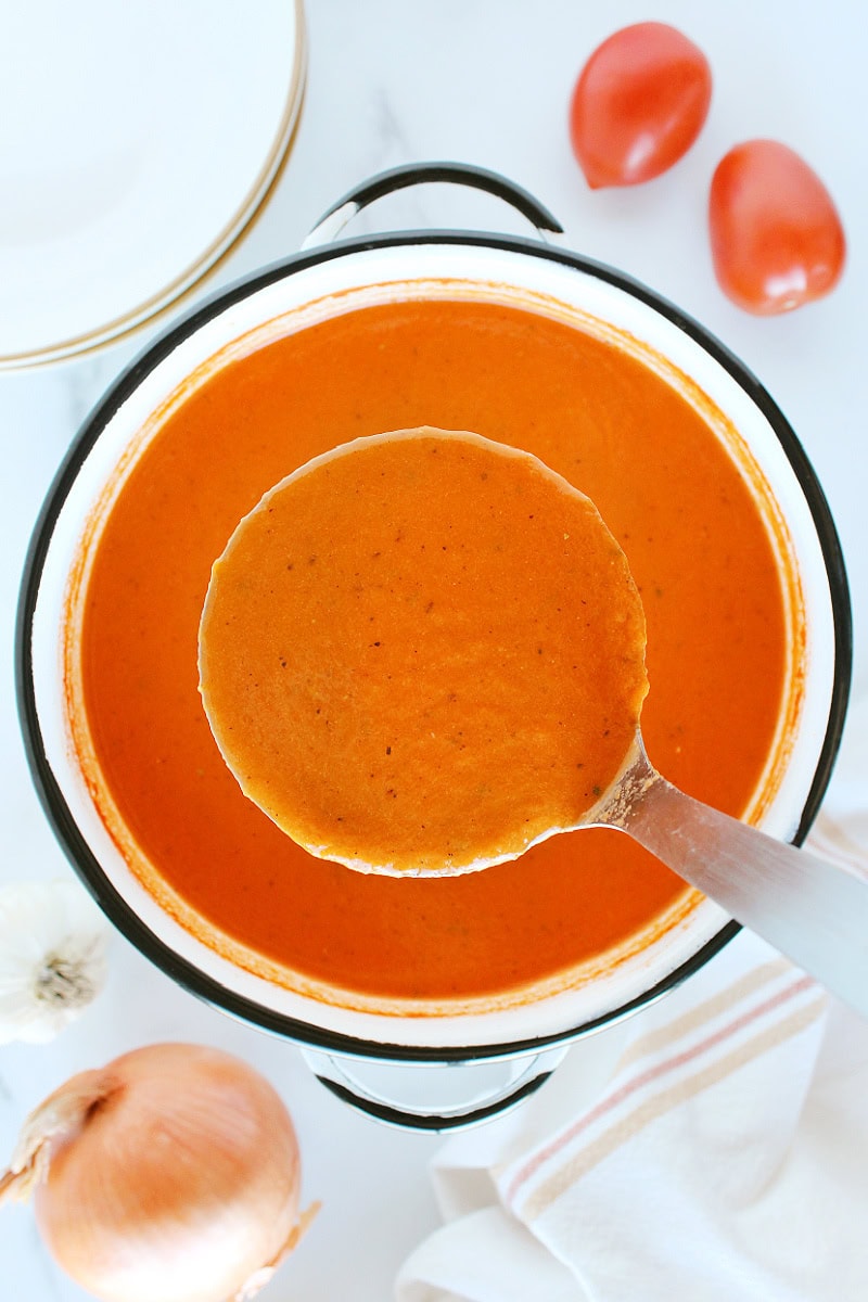 A metal ladle with homemade tomato basil soup over the soup pot.