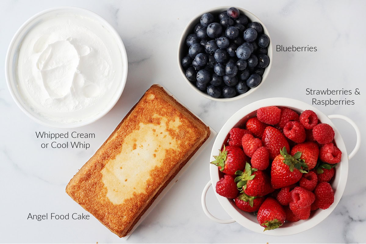 Cool Whip, angel food cake, fresh blueberries, strawberries and raspberries on a white marble countertop.