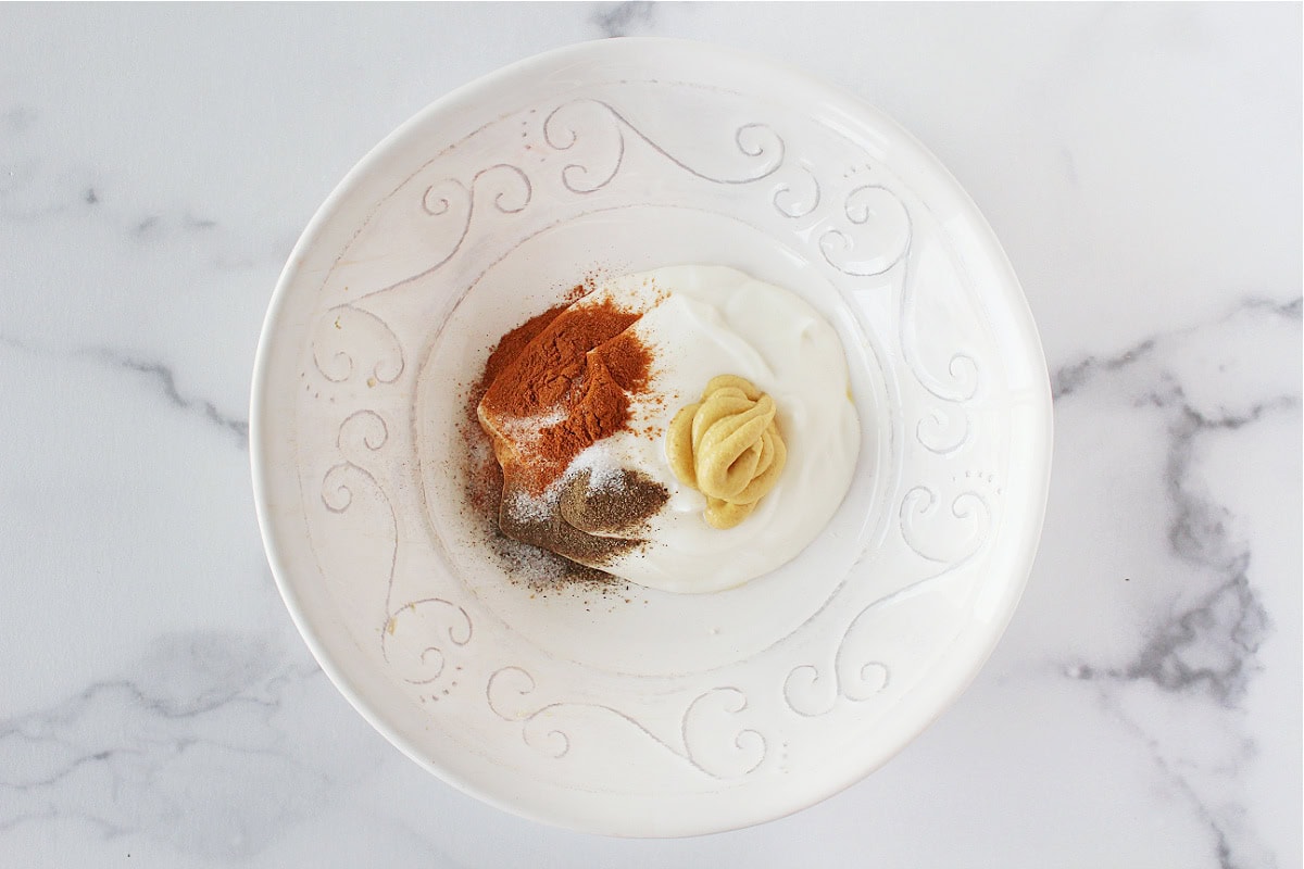 Plain Greek yogurt, Dijon mustard, cinnamon, salt and black pepper in a bowl.