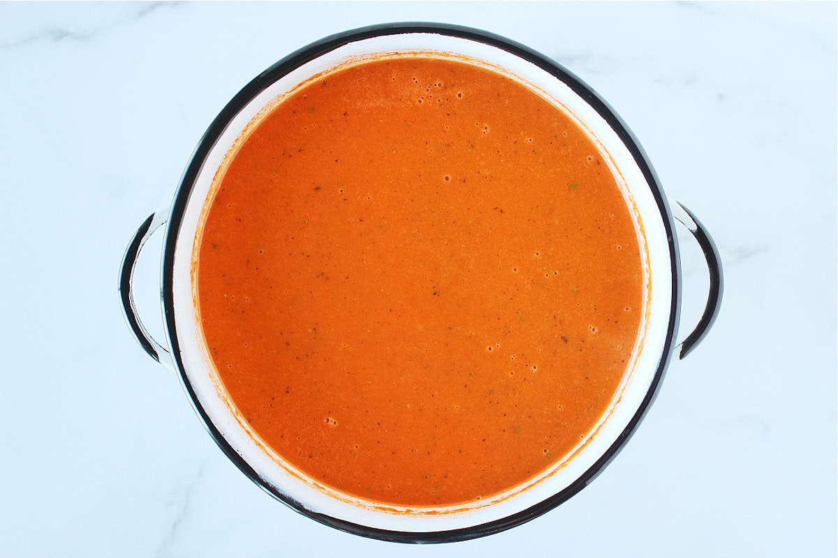 White soup pot filled with creamy tomato soup.