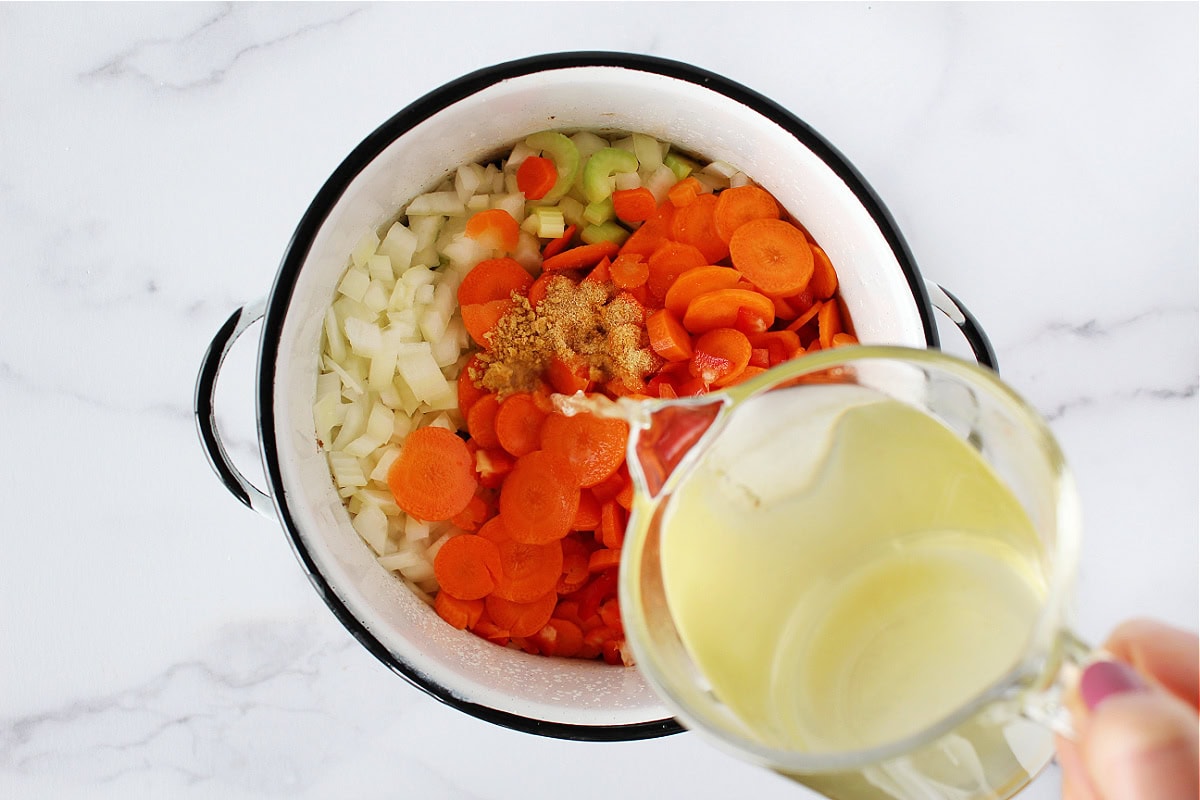 Chicken broth pouring into a pot of veggies.