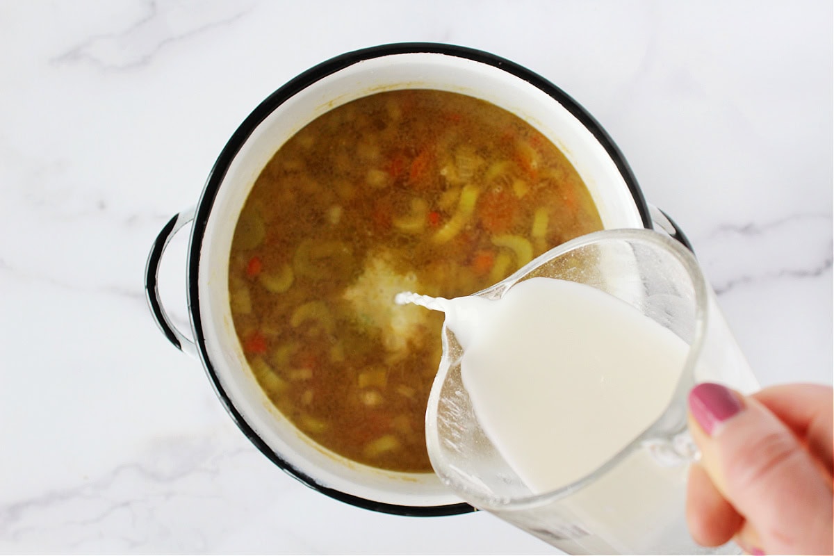 Pouring a slurry mixture of cornstarch and water into a pot of soup.